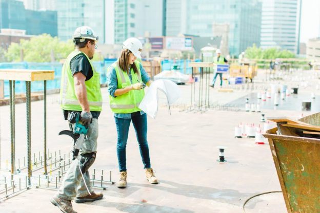 millennial employee looking at plans with foremen on job site